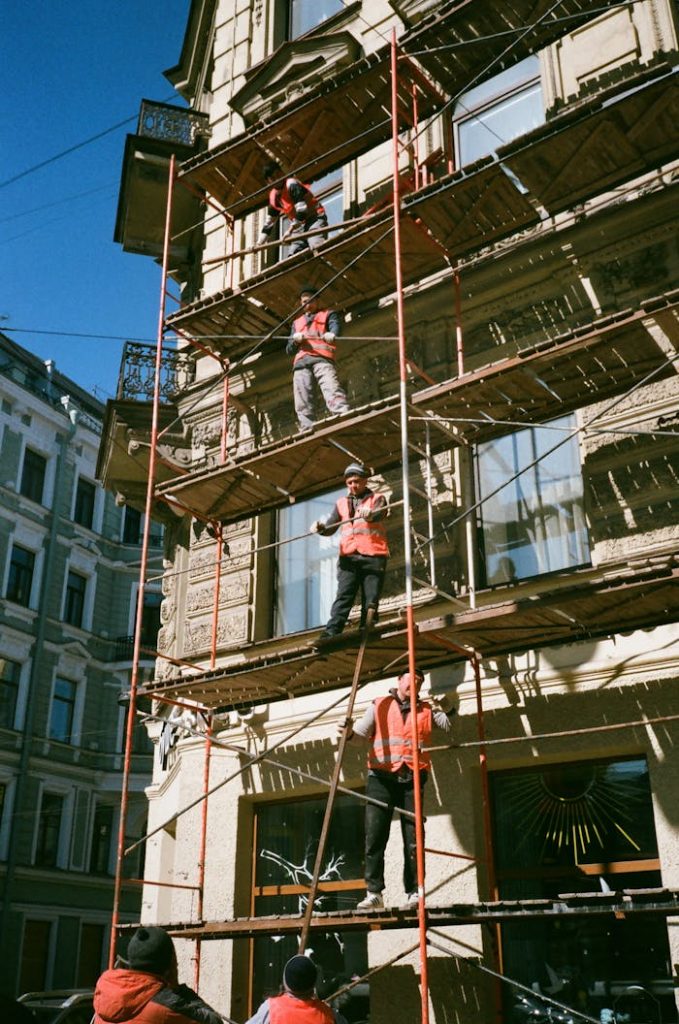 pexels-photo-2209529 Construction workers on scaffolding renovating a building facade on a sunny day.